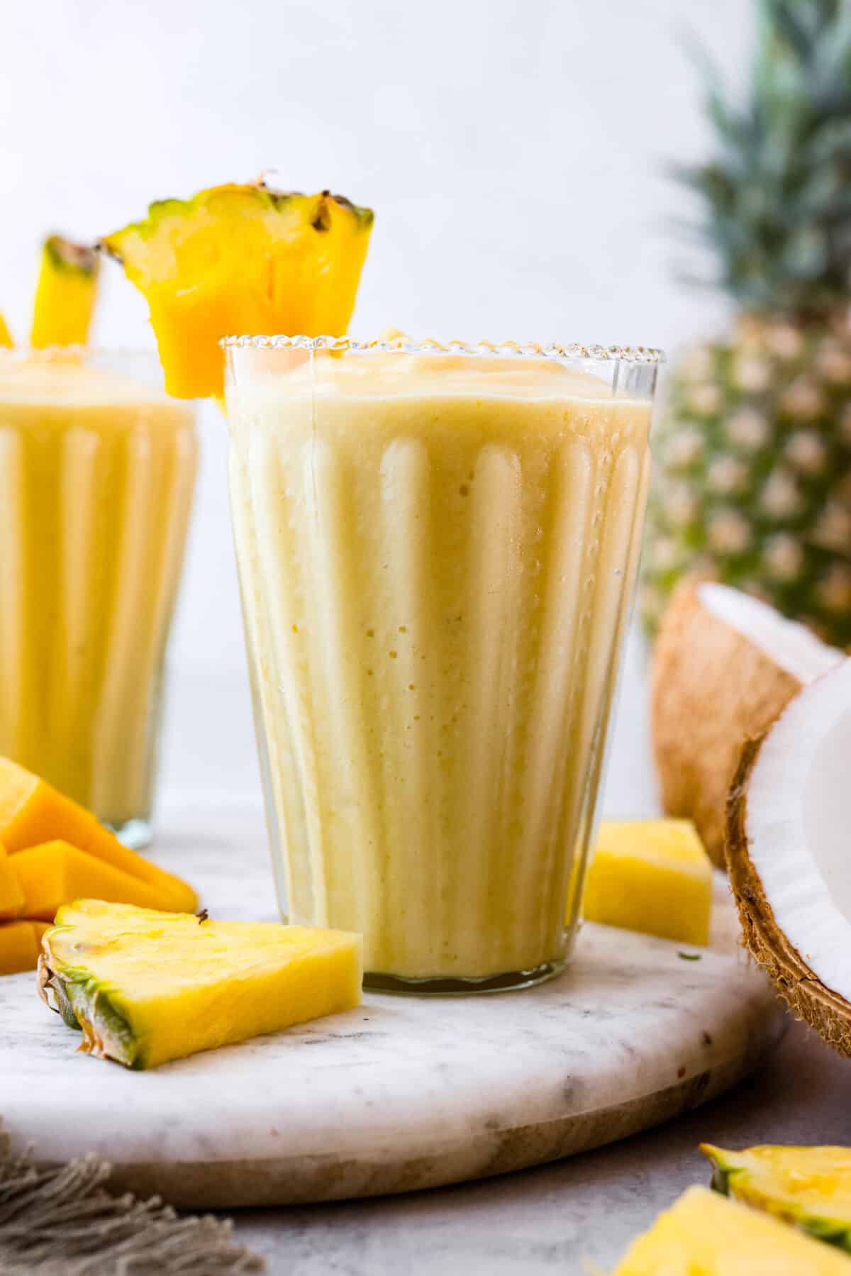 Side shot of glass of tropical smoothie with wedge of pineapple on the rim of the glass. 