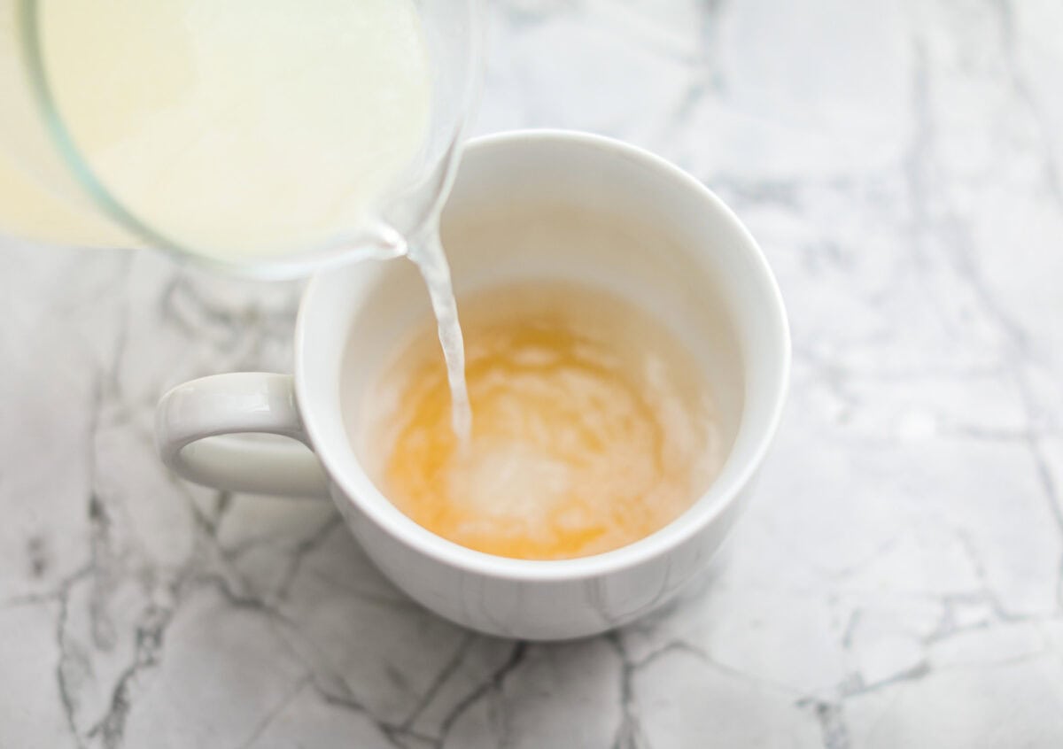 Whenever I am sick, the Starbucks Medicine Ball is my go-to, and this homemade version is even better! Perfect for cold and flu season, this warm drink made of lemonade, honey, and tea is soothing and delicious! Overhead shot of someone pouring the hot lemonade into the mug with the honey.